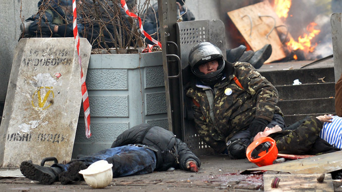 An anti-government protester sit near the bodies of two demonstrators killed by a sniper during clashes with the police in the center of Kiev on February 20, 2014.(AFP Photo / Sergei Supinsky)