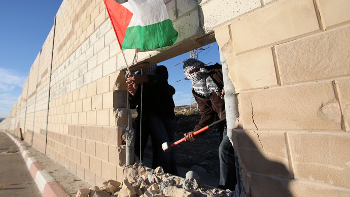 Palestinian youths, one holding a national flag, appear through a hole they dug in the controversial Israeli separation wall in the West Bank village of Bir Nabala -between Jerusalem and Ramallah- on November 8, 2014 as celebrations today mark 25 years since the fall of the Berlin Wall. (AFP Photo)