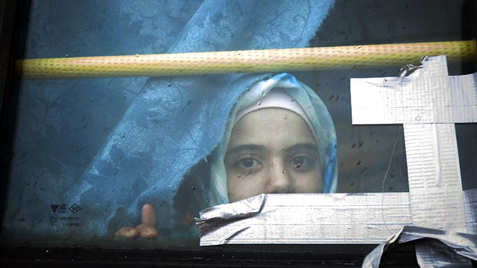A Syrian girl looks through the window of a bus where she has lived with her family for the past eight months at a refugee camp in Bab al-Salam on the Syria-Turkey border. (AFP Photo / Bruno Gallardo)
