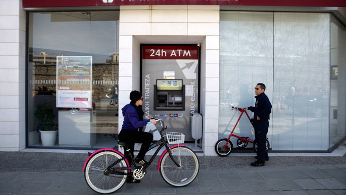 A woman rides her bike past a Laiki (Popular) Bank branch on March 25, 2013 in Nicosia.(AFP Photo / Yiannis Kourtoglou)
