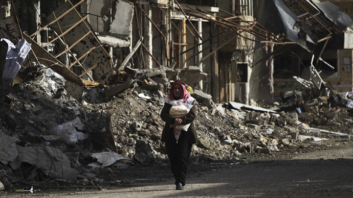 A man holds bread as he walks along a damaged street filled with debris in Deir al-Zor, eastern Syria February 19, 2014 (Reuters/Khalil Ashawi)