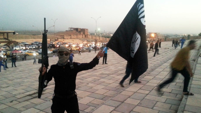 A fighter of the Islamic State of Iraq and the Levant (ISIL) holds an ISIL flag and a weapon on a street in the city of Mosul, June 23, 2014. (Reuters / Stringer)
