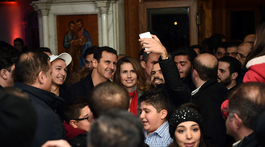 Syrian President Bashar Assad (C-L) and his wife Asma al-Assad (C-R) posing for a picture with a Syrian man as they attend a Christmas choral presentation at the Lady of Damascus Catholic Church in the Syrian capital on December 18, 2015. © HO