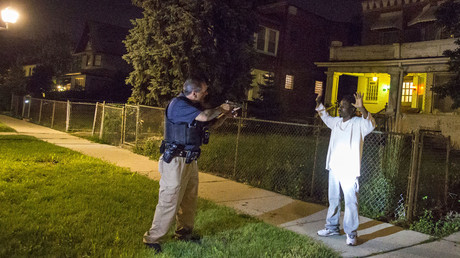 A Cook County Sheriff police officer (L) points his gun at a man who walked up to him while officers were conducting an unrelated street stop in the Austin neighborhood in Chicago, Illinois, United States, September 9, 2015. © Jim Young