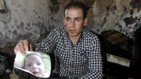 A relative of 18-month-old Palestinian baby Ali Dawabsheh, who was killed after his family's house was set to fire in a suspected attack by Jewish extremists, shows his picture at the burnt house in Duma village near the West Bank city of Nablus July 31, 2015 © Abed Omar Qusini
