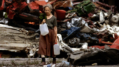 An elderly woman carrying stream water trudges through an area exposed to sniper fire in the besieged capital. © Chris Helgren