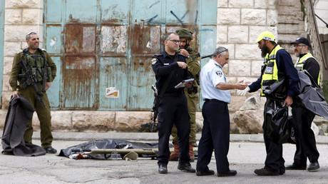 Israeli security forces inspect the scene as the dead body of one of two Palestinians, whom the Israeli military said were shot dead by Israeli troops after they attacked an Israeli soldier, is covered in Tal Rumaida in the West Bank city of Hebron March 24, 2016. © Mussa Qawasma