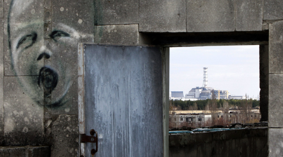 The sarcophagus covering the damaged fourth reactor at the Chernobyl nuclear power plant is seen behind a building decorated with a graffiti in the abandoned city of Prypiat. © Gleb Garanich