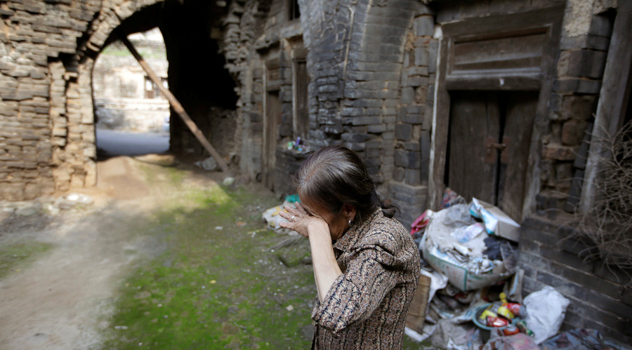 Li Yonghua, 65, wipes her eyes in front of her damaged cave house in an area where land is sinking next to a coal mine, in Helin village of Xiaoyi, China's Shanxi province, August 2, 2016. © Jason Lee