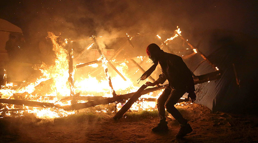 A migrant is seen in silhouette near flames from a burning makeshift shelter on the second day of the evacuation of migrants and their transfer to reception centers in France, as part of the dismantlement of the camp called the "Jungle" in Calais, France, October 25, 2016. © Neil Hall