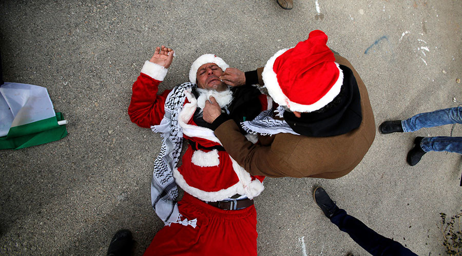 A man tends to a Palestinian protester, dressed as Santa Claus, after inhaling tear gas fired by Israeli troops during clashes in the West Bank city of Bethlehem, December 23, 2016. © Mussa Qawasma 