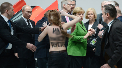 A topless dAemonstrator with a message on her back walks towards Russian President Vladimir Putin (L) and German Chancellor Angela Merkel (C) during their visit of the Hanover industrial Fair in Hanover, central Germany, on April 8, 213.  (AFP Photo/Jochen Lübke)