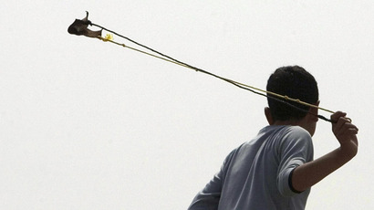 A Palestinian boy uses a sling to hurl a stone towards Israeli soldiers during a protest against Israel's security barrier in the West Bank village of Bilin near Ramallah (Reuters)