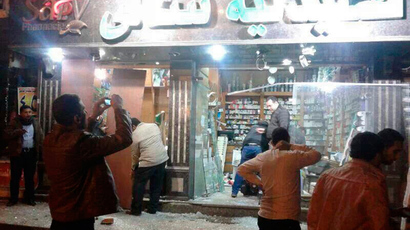 People walk around a damaged shop after an explosion at a security building in Mansoura city, the capital of Dakahlyia Governorate, about 120 km (75 miles) northeast of Cairo, December 24, 2013. (Reuters / Stringer
