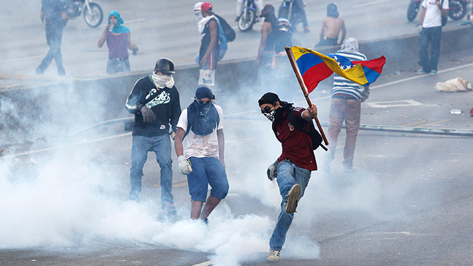 An anti-government protester, with the Venezuelan flag, kicks back a gas canister to police during a demonstration in which masked youths battled police and blocked a main highway in Caracas April 21, 2014 (Reuters / Christian Veron)