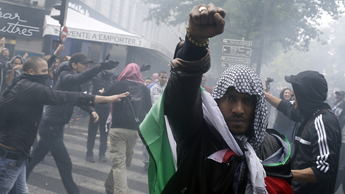 A protester wearing a kaffiyeh and wrapped in a Palestinian flag raises his fist on July 13, 2014 in Paris. (AFP Photo / Kenzo Tribouillard)